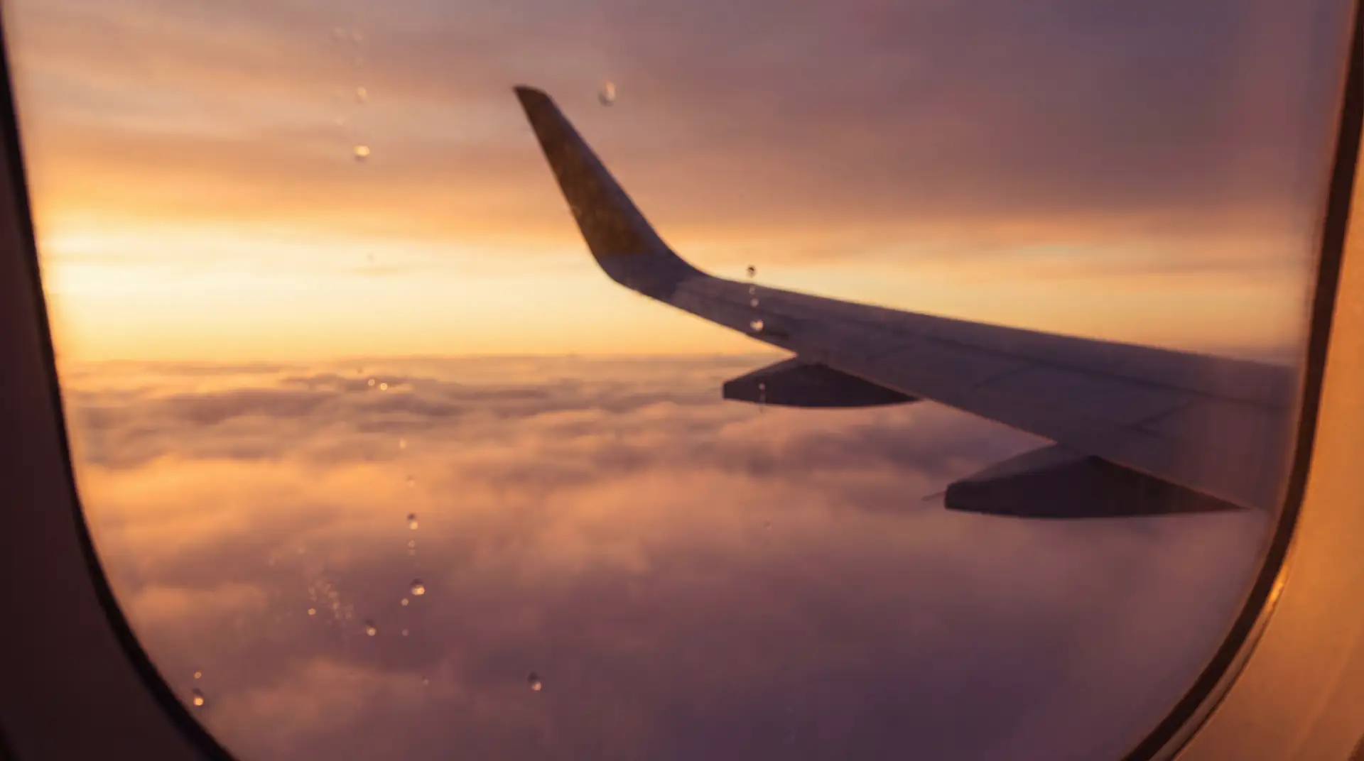 Airplane window view above clouds at golden hour sunset — OraVisa travel and visa guides from Dubai